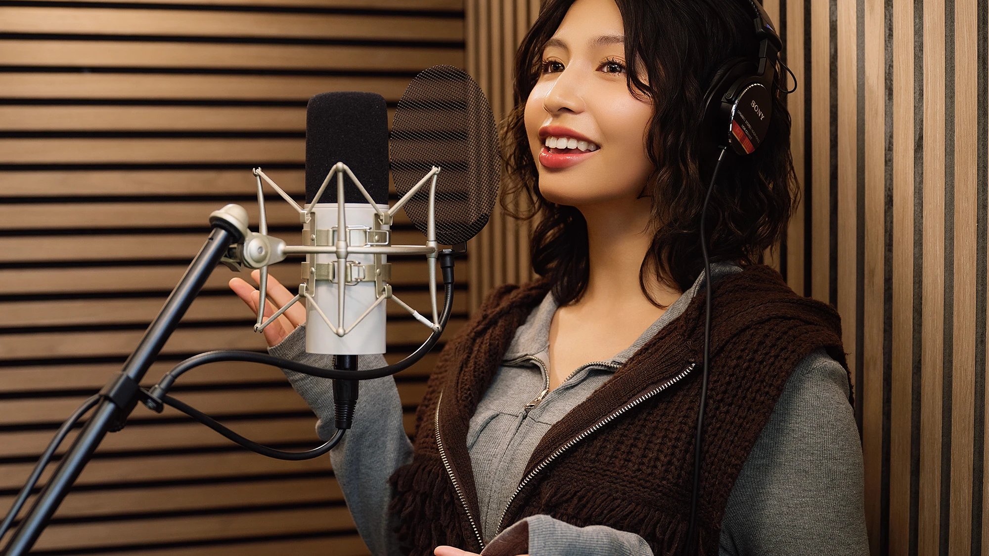 A singer smiling at the studio microphone inside the booth